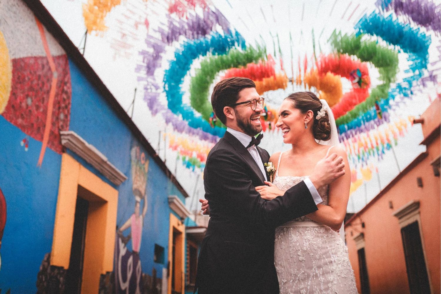 A couple shares a romantic moment under vibrant rainbow tinsel decorations at an outdoor wedding celebration.