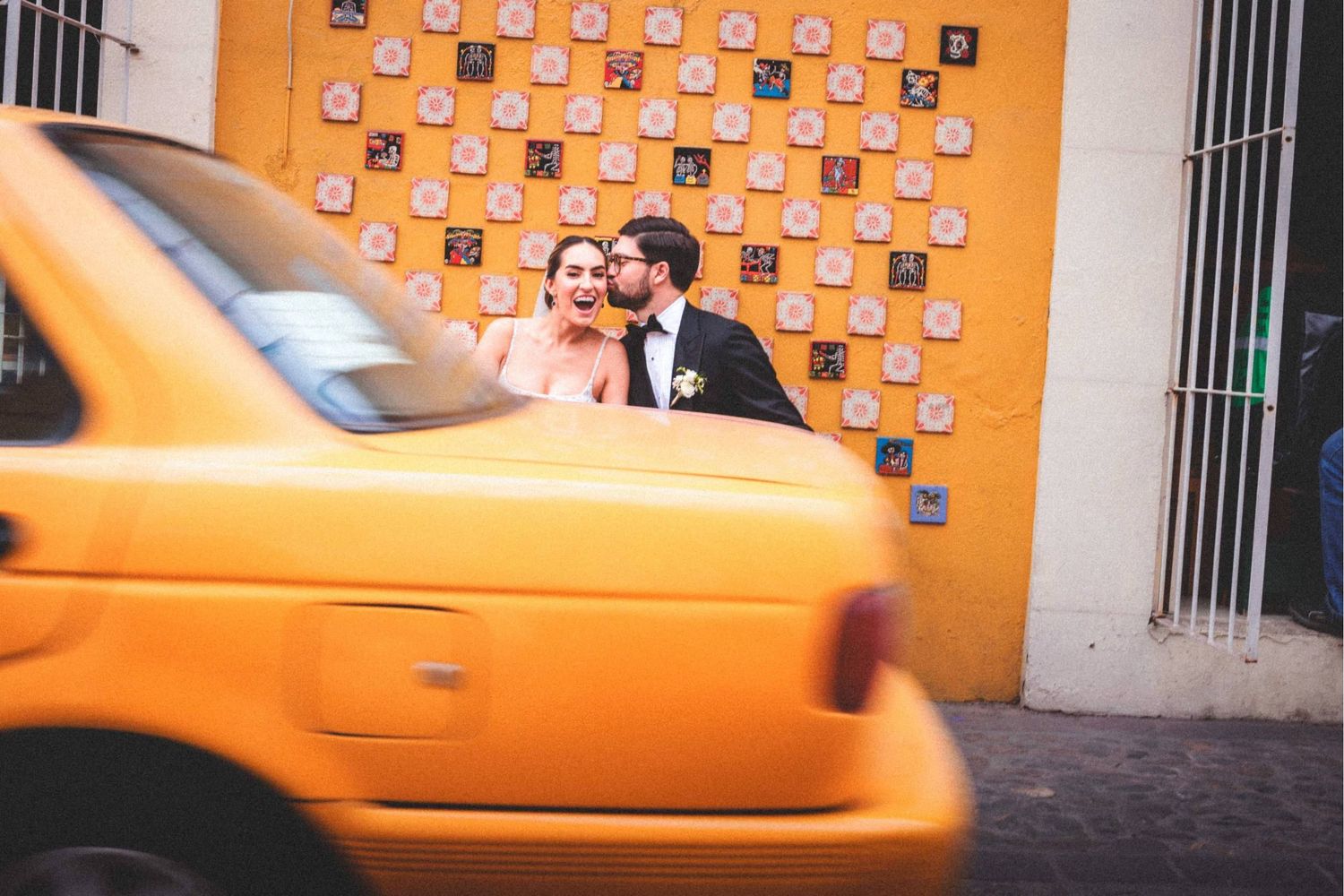 A sequence of yellow taxi cabs lined up on a street with framed photos hanging on an orange wall.