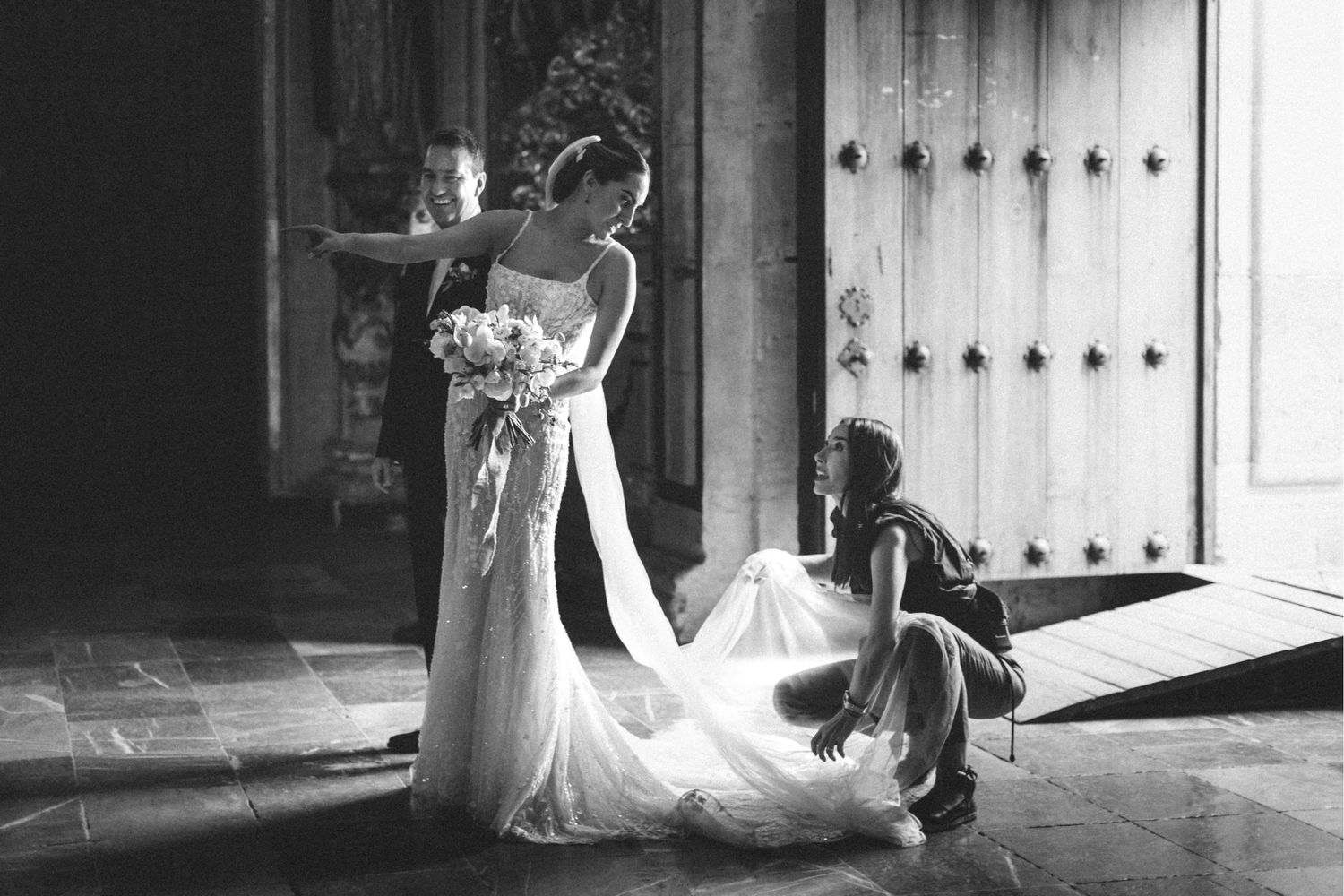 A wedding couple stands silhouetted in dramatic window light creating a romantic black and white portrait.