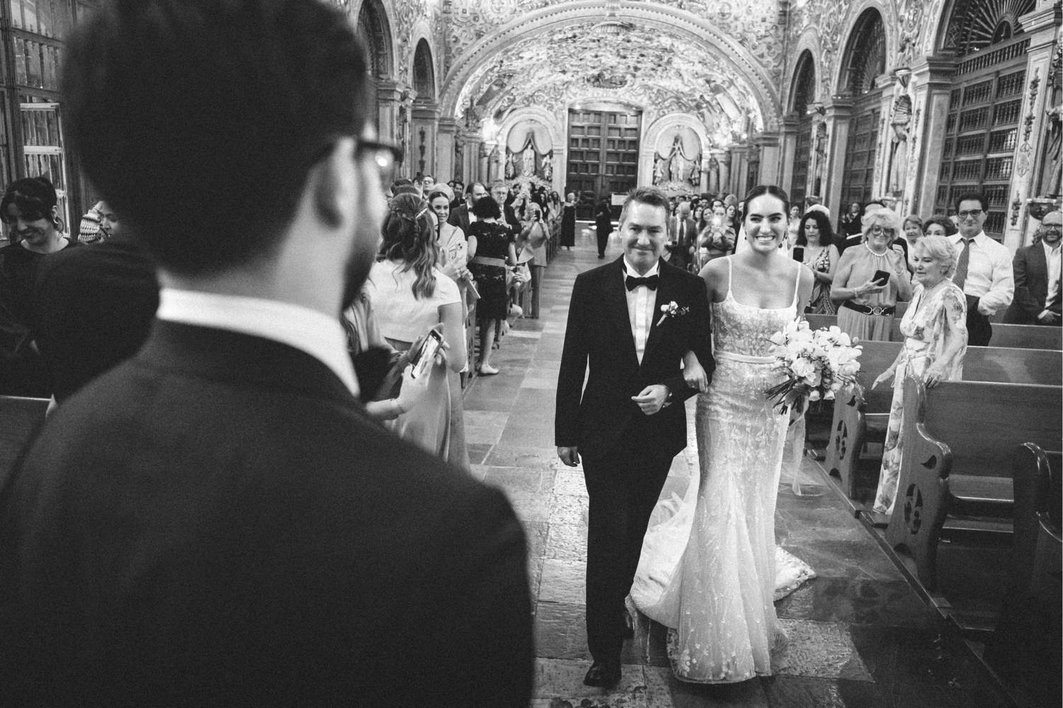 A wedding party walks down a church aisle during a traditional ceremony with guests watching from the pews.