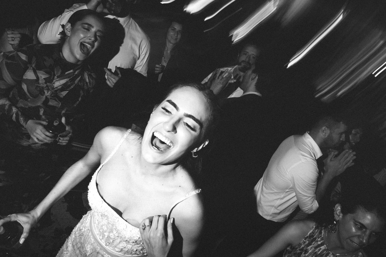 Black and white photo of people dancing and laughing at a nightclub with motion blur effects.