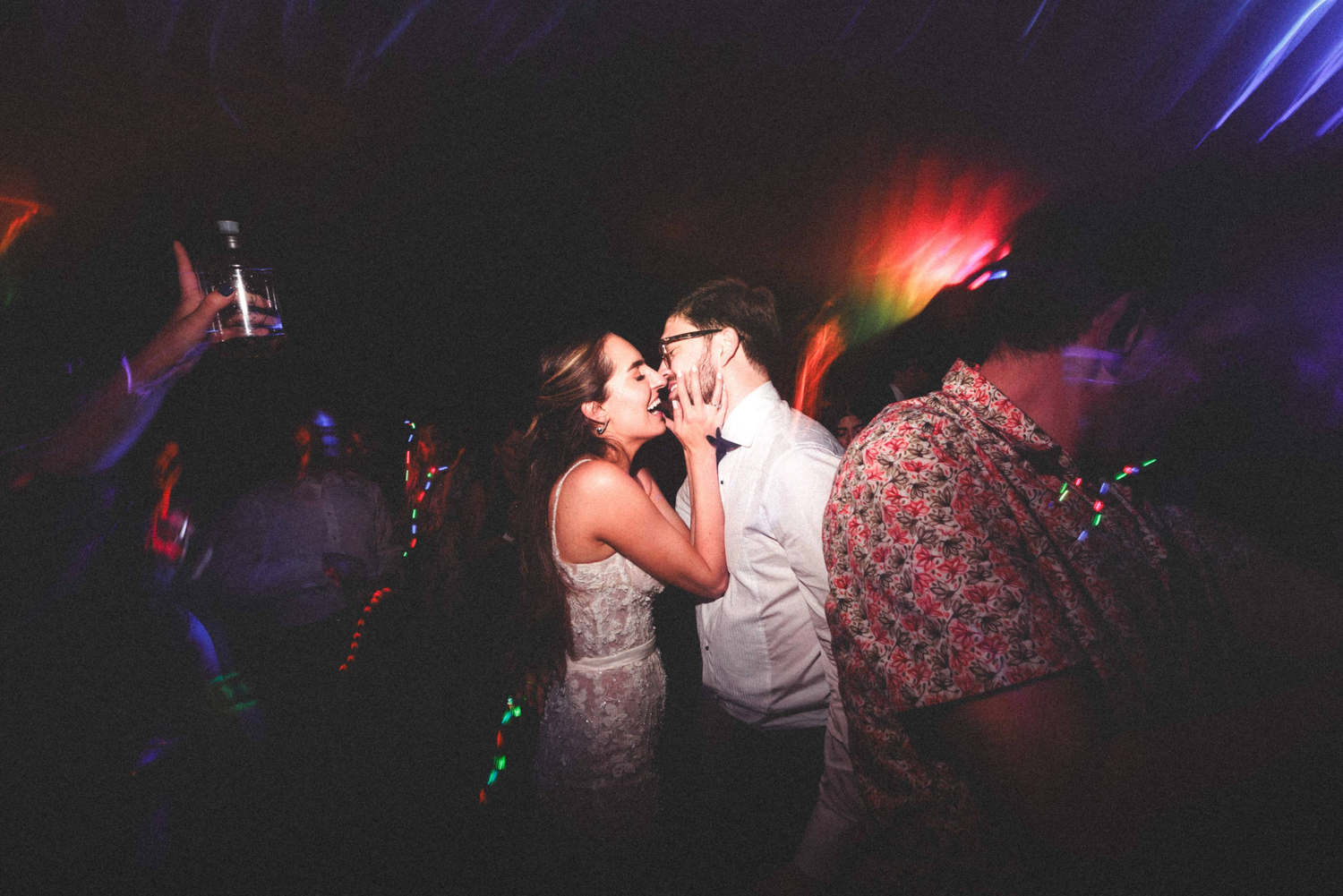 Couples dance together on a dark dance floor illuminated by colorful purple and red lighting effects.
