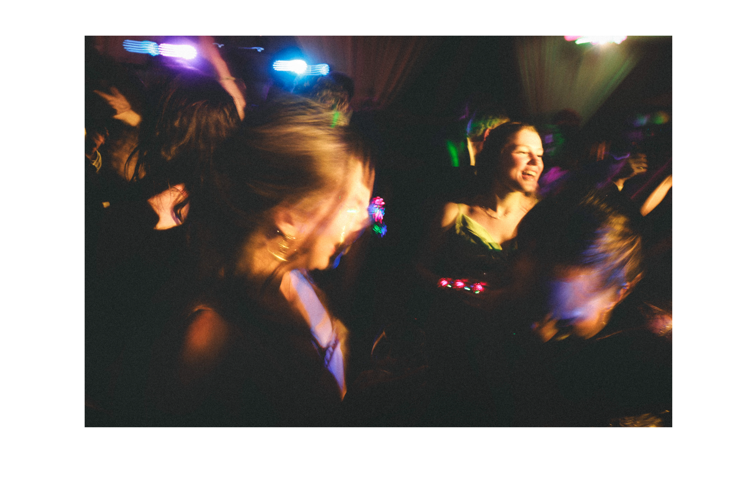 People dancing and moving in a dark nightclub with colorful lighting and blurred motion effects.