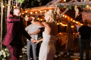A couple shares their first dance at a rustic barn wedding reception with warm string lights glowing overhead.