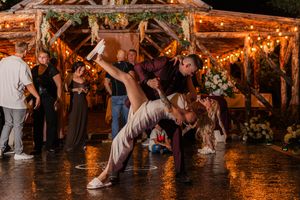 Wedding reception guests dance on a glowing wooden floor under warm string lights at an outdoor evening celebration.