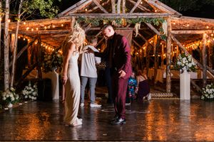 People dance and celebrate on a rustic wooden dance floor illuminated by warm string lights at a barn wedding reception.