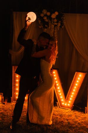 Large illuminated marquee letters spelling LOVE glowing warmly against a dark outdoor wedding setting.