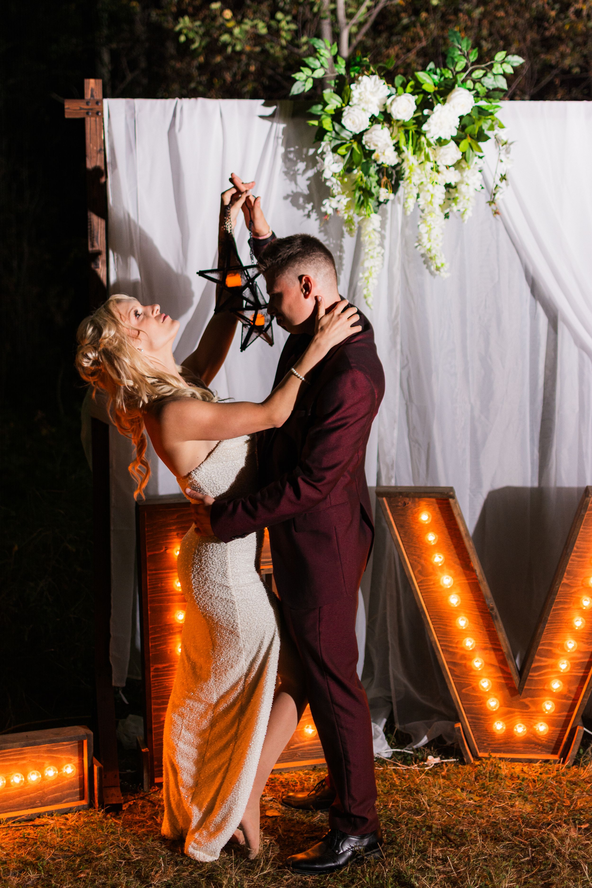 A couple shares a romantic moment in front of illuminated marquee letters at an elegant wedding reception.