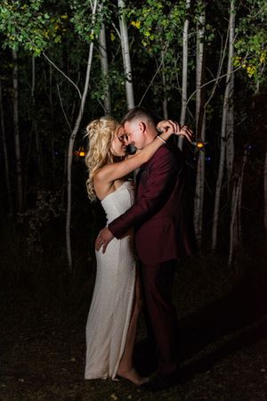 A romantic embrace between newlyweds in a wooded setting with string lights.