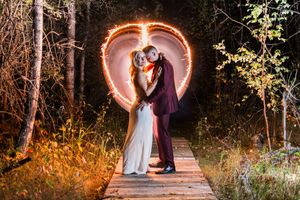 Romantic evening outdoor wedding portraits along a wooden pathway illuminated by string lights.