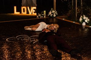 A creative wedding photo with couple lying on dance floor beneath illuminated LOVE sign.