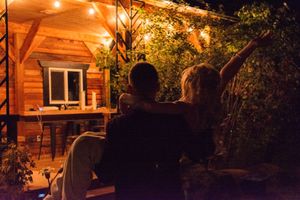 People enjoying an evening gathering on a wooden deck illuminated by warm ambient lighting.