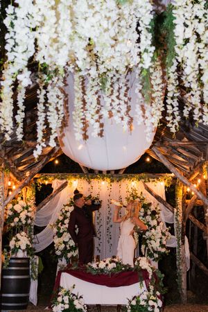 Elegant wedding venue ceiling adorned with cascading white floral arrangements and draped fabric under warm lighting.