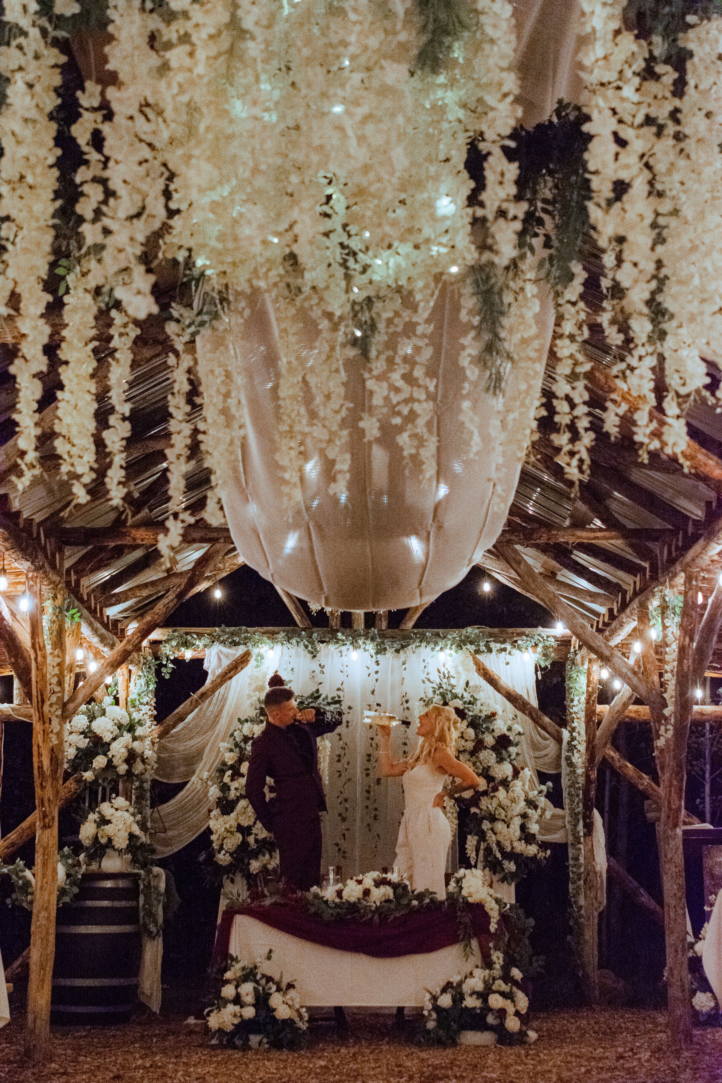 A romantic outdoor wedding venue decorated with cascading white flowers and draped fabric creating an ethereal atmosphere.