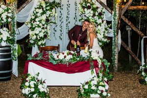 Wedding ceremony arch decorated with lush white floral arrangements and greenery in an outdoor setting.