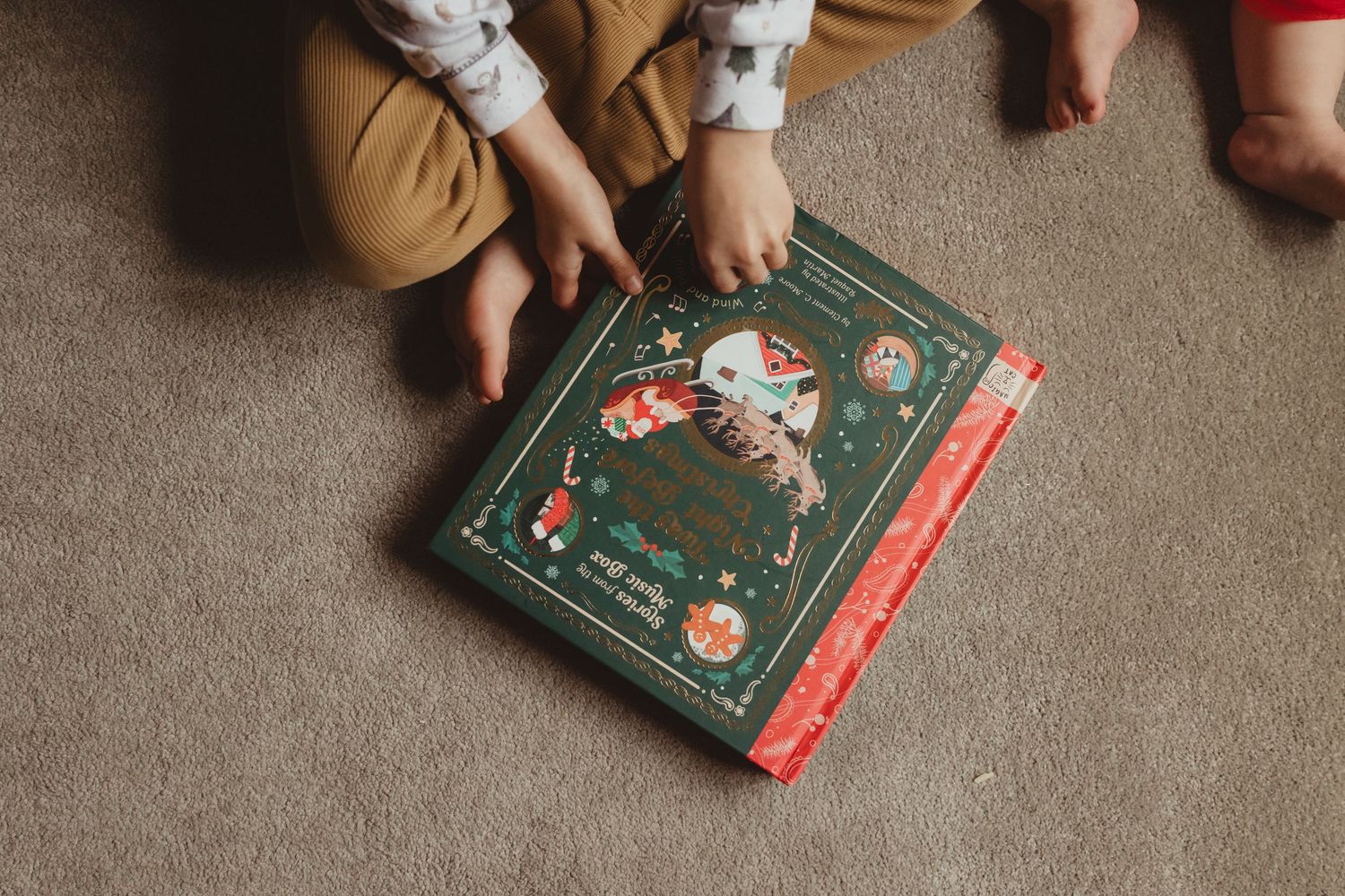 Small feet rest near a vintage-style green and red Christmas storybook on beige carpet.