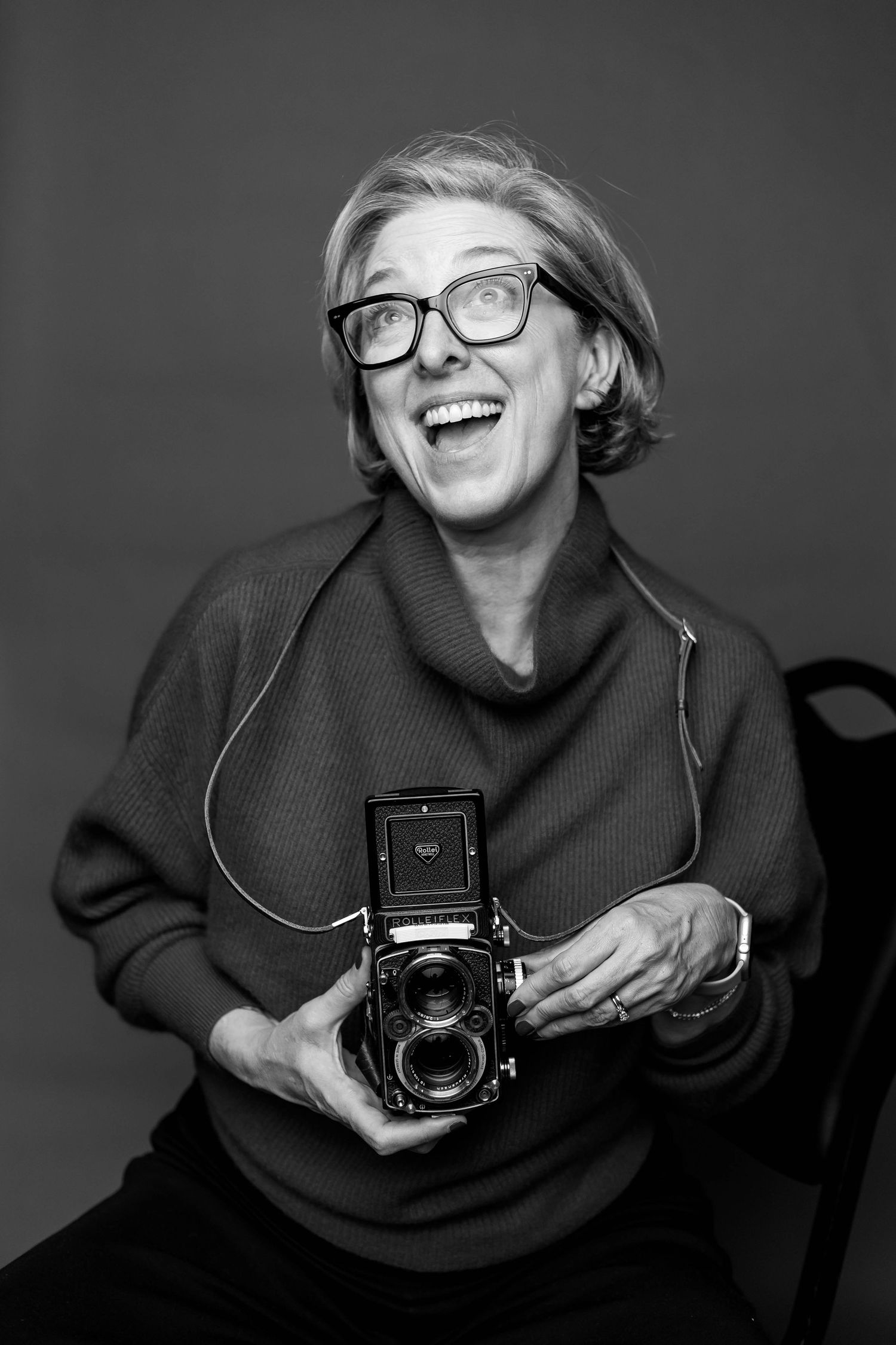 Black and white photo of a photographer laughing while holding a vintage medium format camera.