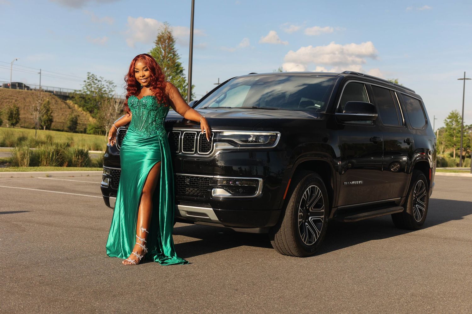 Woman in emerald green sequin gown with thigh slit poses elegantly beside black Jeep Wagoneer SUV.