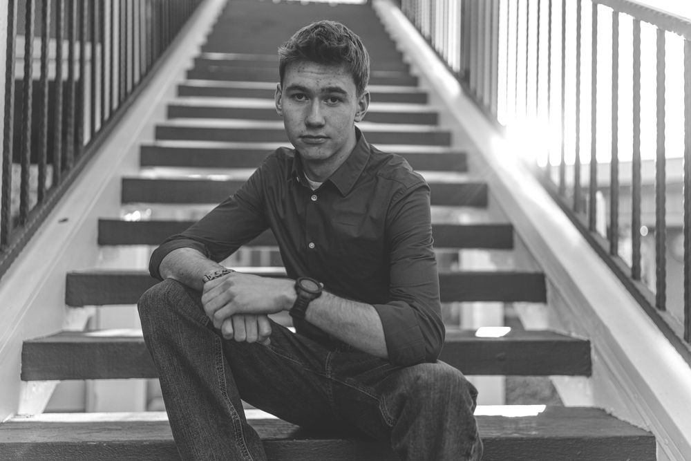 Black and white portrait of musician sitting on concrete steps with railing.