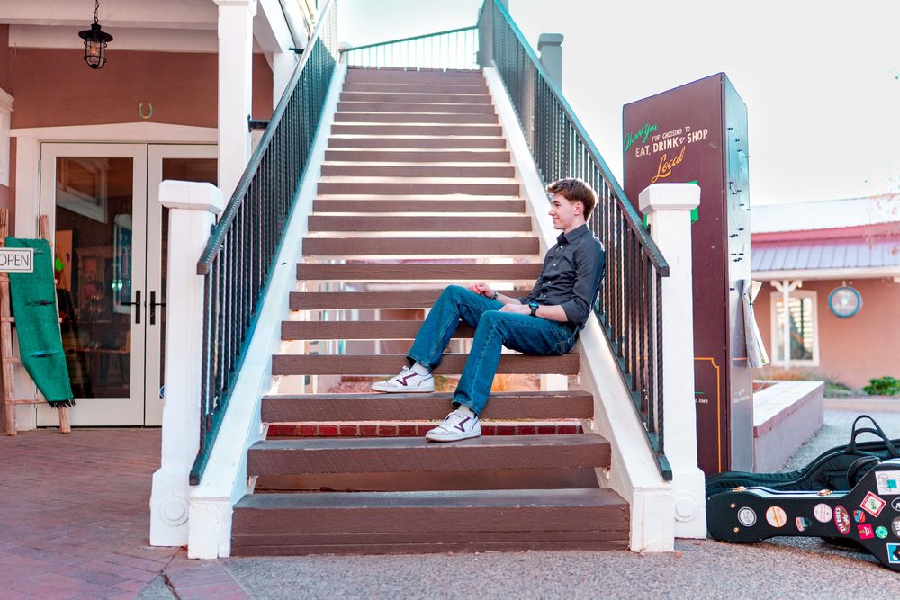Musician sitting casually on outdoor staircase with white railings.