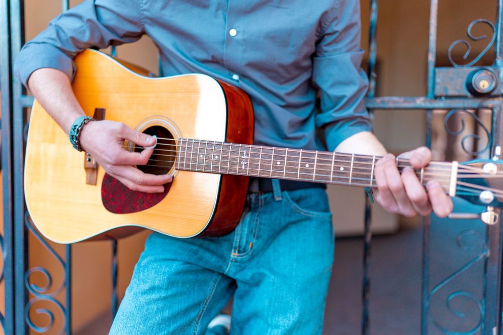 Close up of hands playing acoustic guitar wearing blue shirt and jeans.
