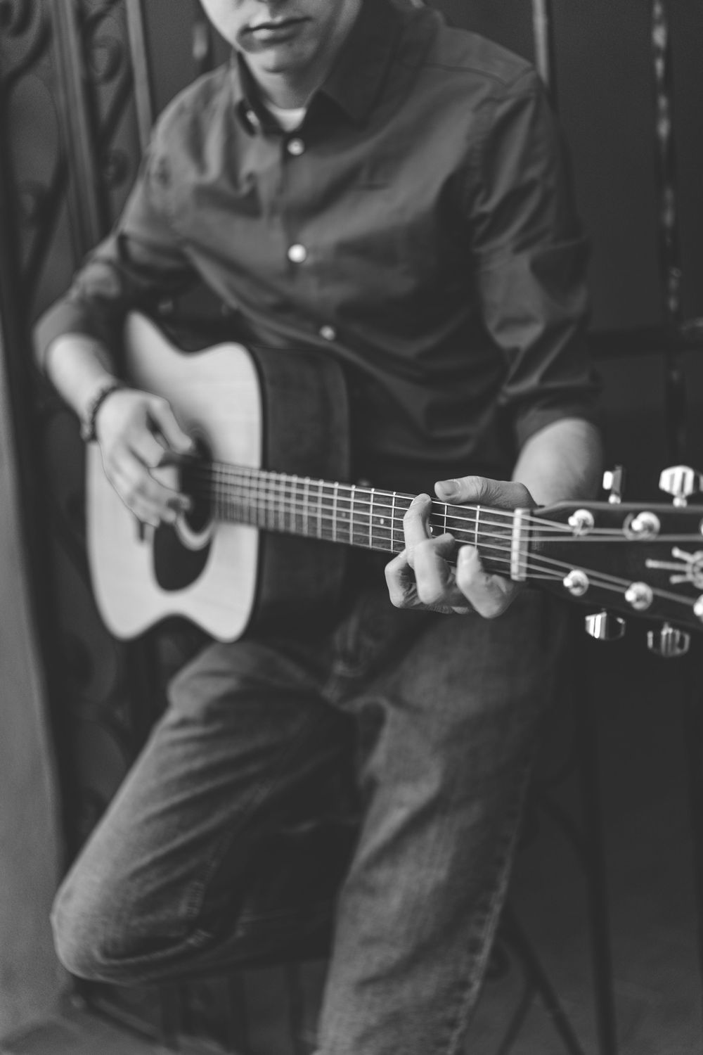 Black and white close-up of acoustic guitar being played with detailed finger positioning.