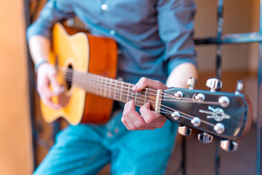 Close-up of hands playing acoustic guitar showing proper finger positioning on fretboard.