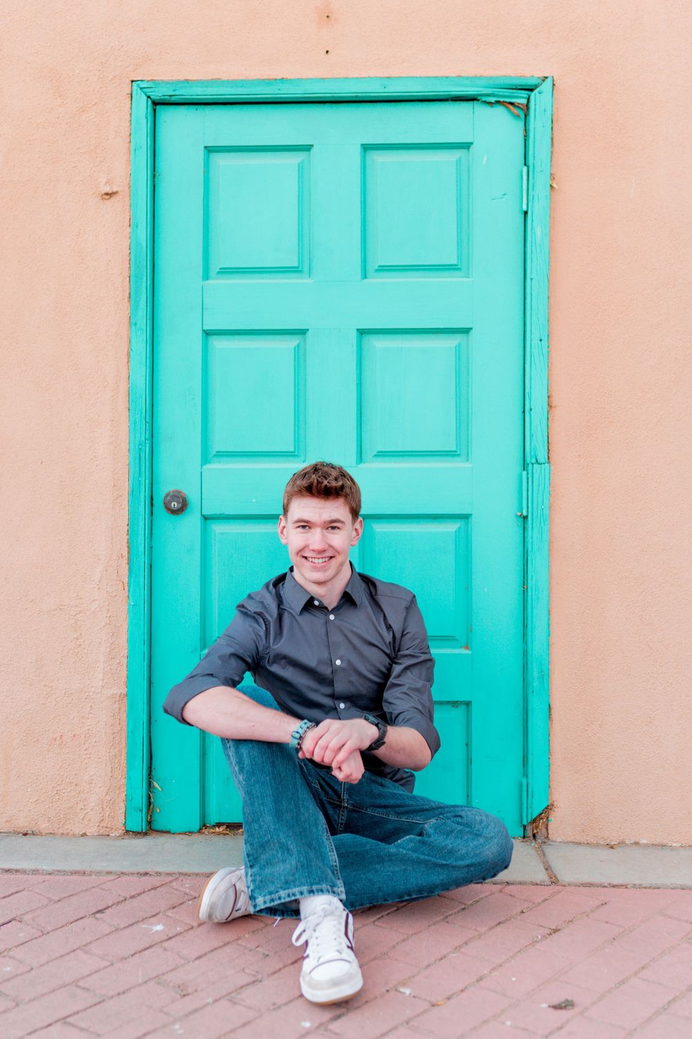 Person sitting casually in front of vibrant turquoise door on peach-colored wall.