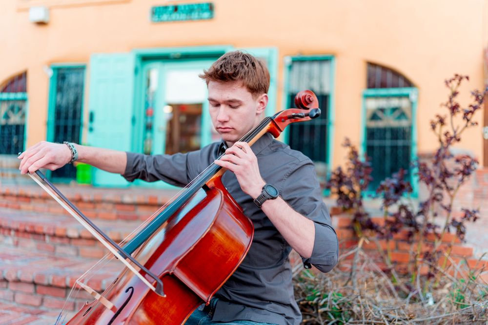 Musician playing cello outdoors against southwestern architecture with turquoise accents.