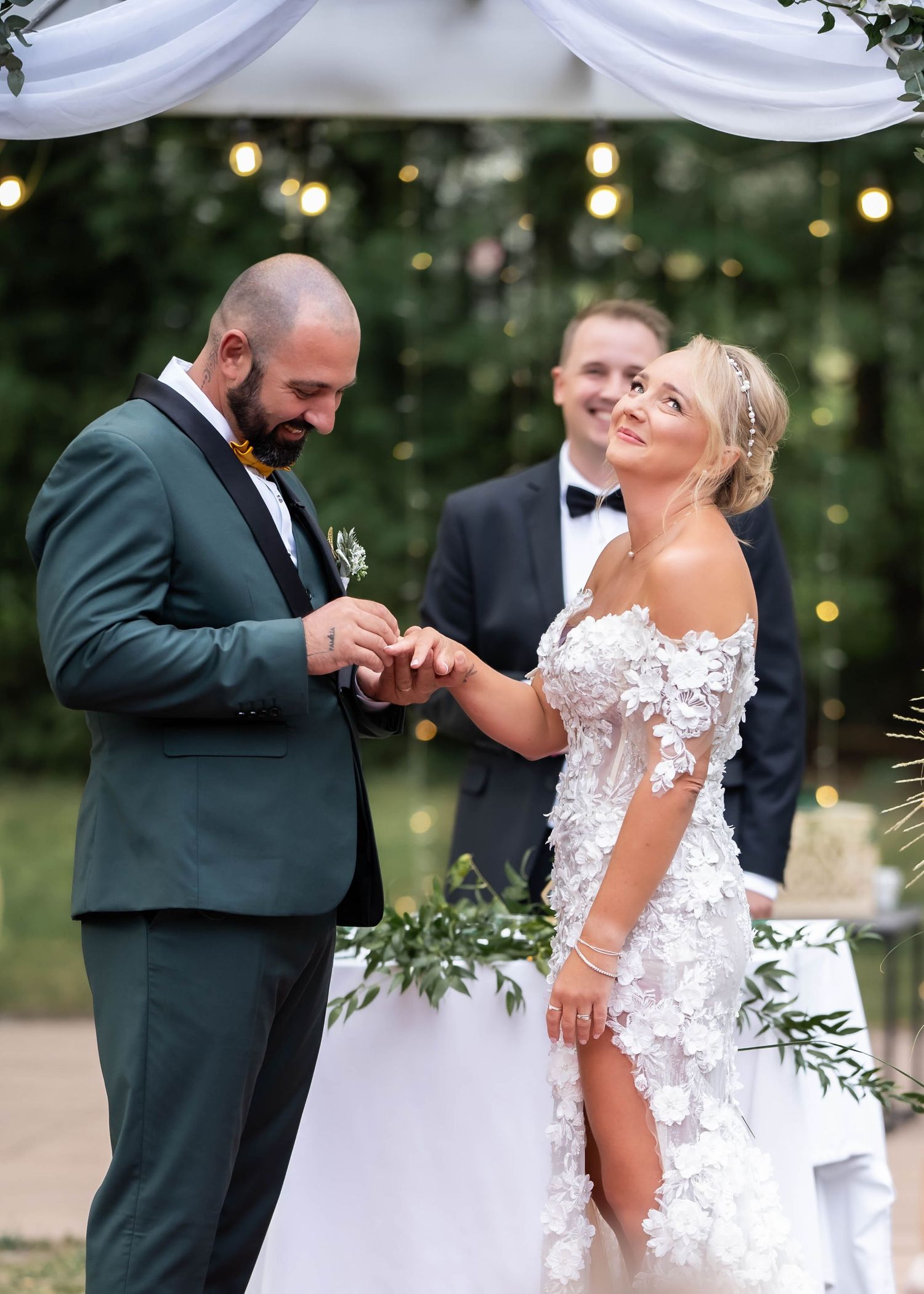 Outdoor wedding ceremony moment with couple exchanging rings under string lights.