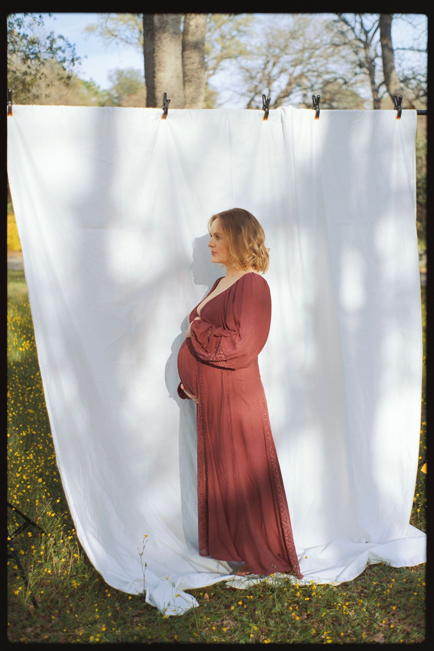 Side profile maternity photo against white backdrop with burgundy maxi dress.