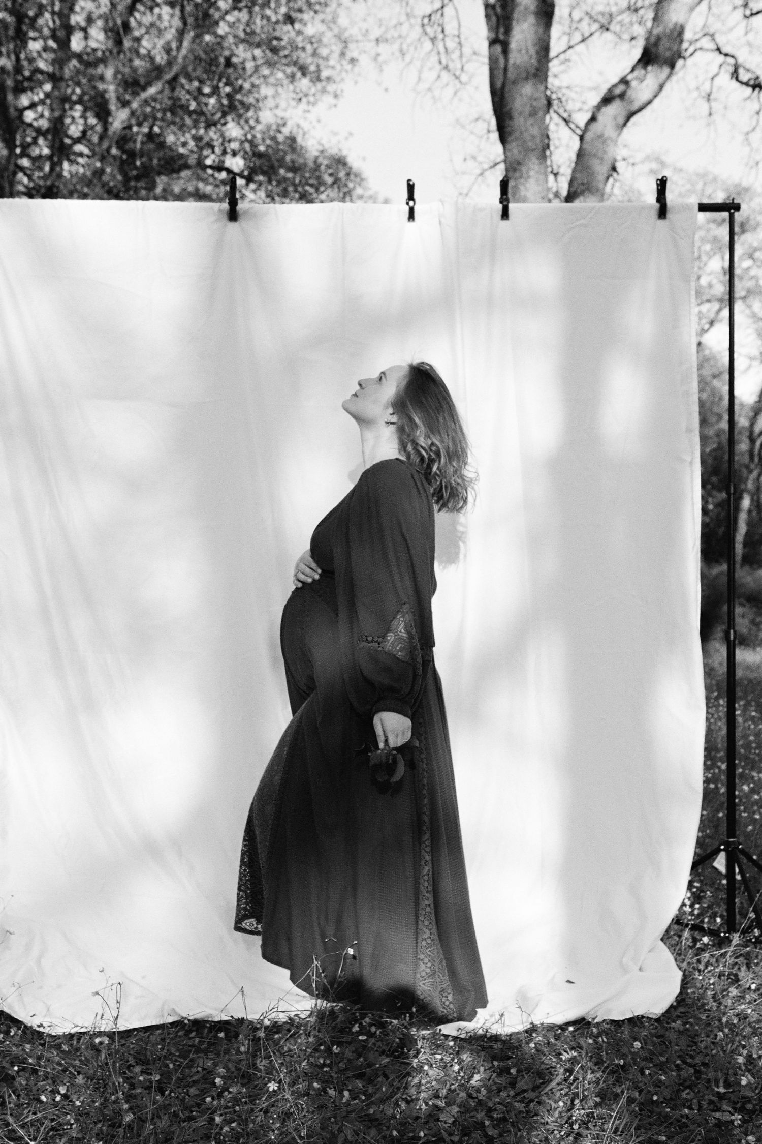Artistic black and white maternity silhouette against white backdrop outdoors.