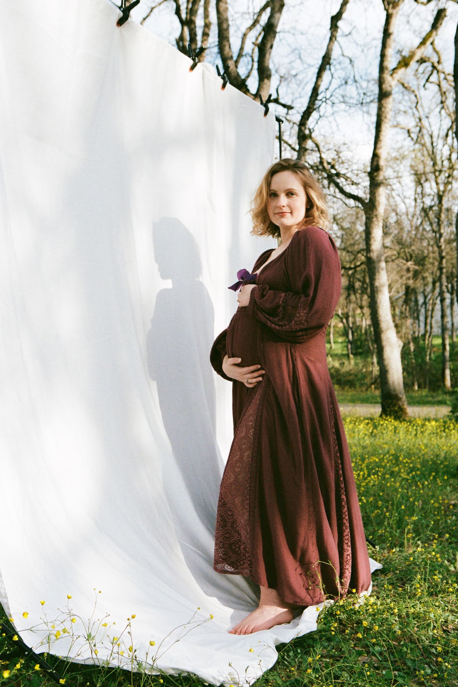 Maternity portrait against white backdrop with burgundy dress in natural setting.