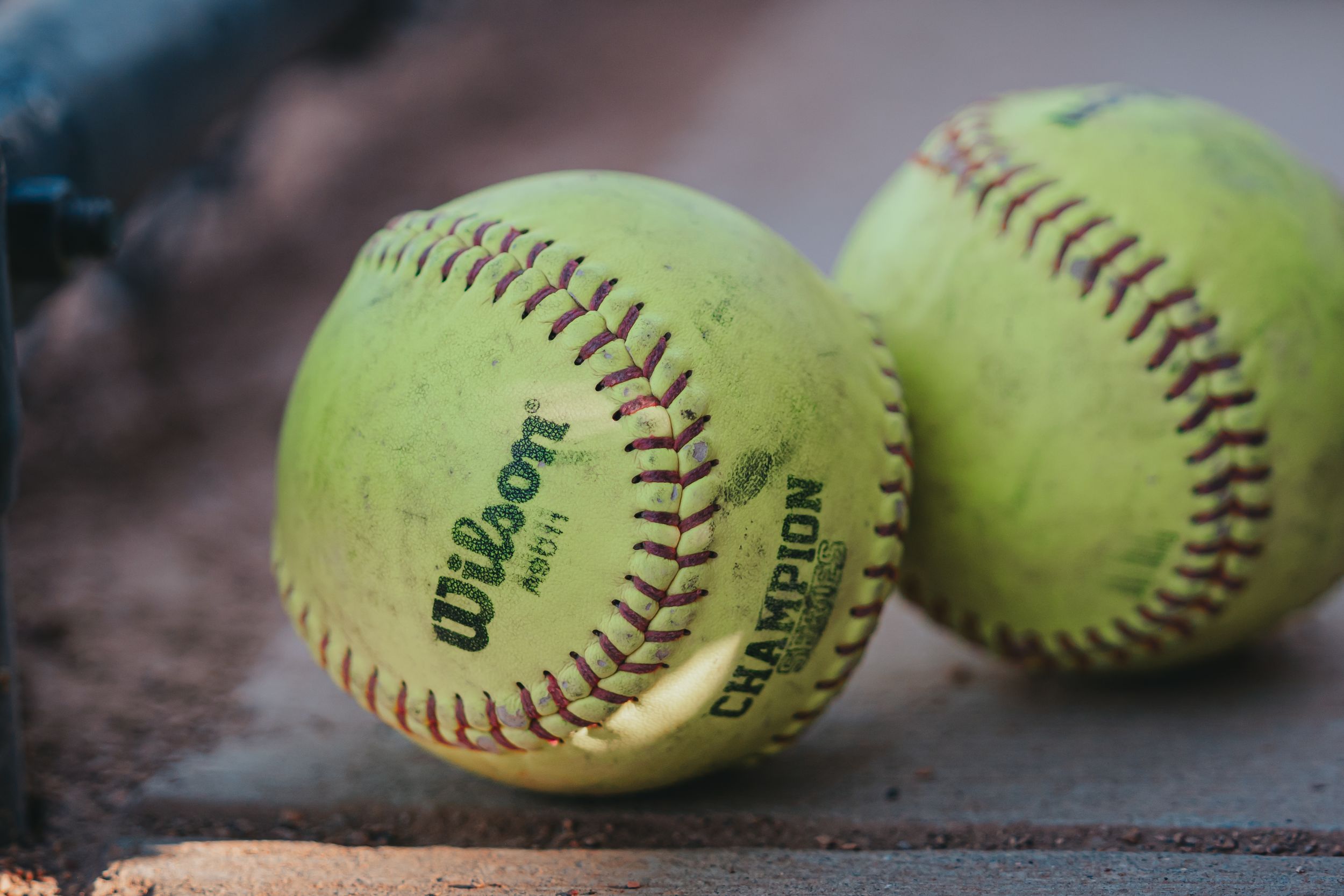 Dynamic Sports Photography of two yellow softballs with red stitching rest on a wooden surface - Warsaw, Indiana