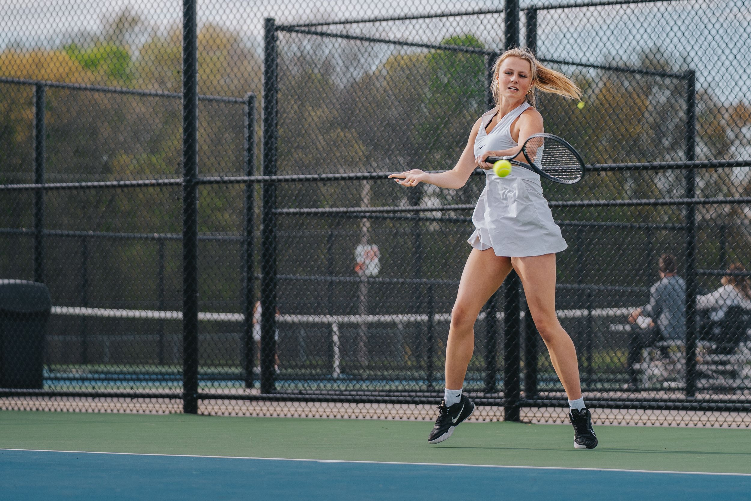 Sports Photography of a tennis player mid-serve on an outdoor court with chain link fencing in the background - Warsaw, Indiana