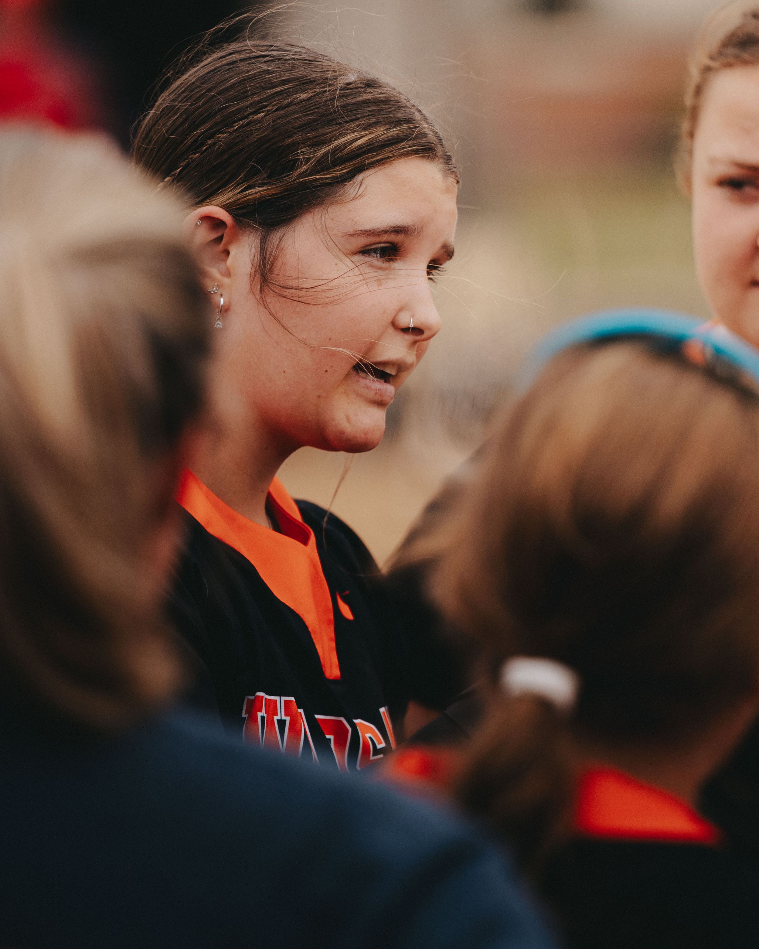 Sports Photography of a team huddle discussion during softball game with players in orange jerseys - Warsaw, Indiana