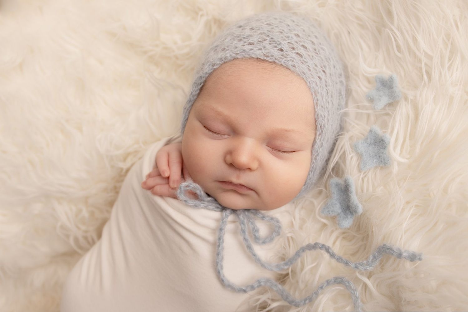 Peaceful sleeping newborn wearing soft gray bonnet rests on cream-colored blanket with blue accents.