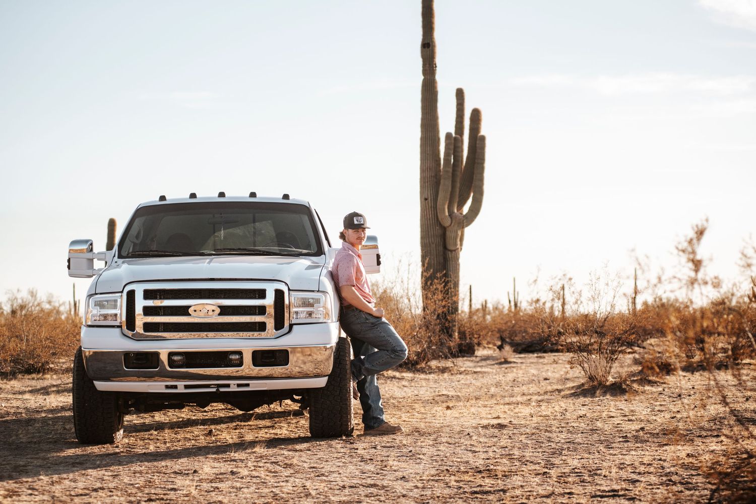 A silver Ford pickup truck posed in front of a tall saguaro cactus in the desert landscape.