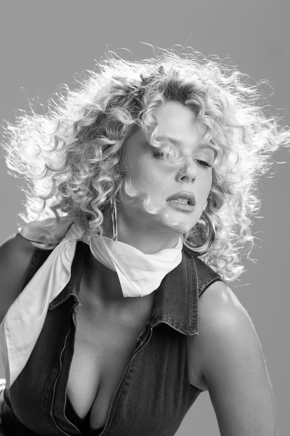 Black and white portrait showing wild curly blonde hair and dramatic lighting against dark background.