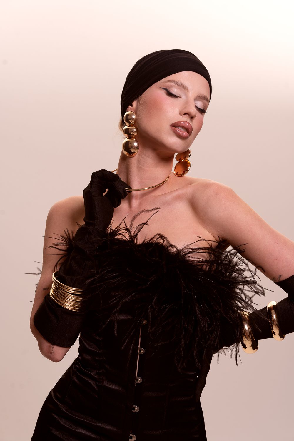 Fashion portrait featuring a glamorous black velvet dress with feathers, statement gold jewelry and long gloves.