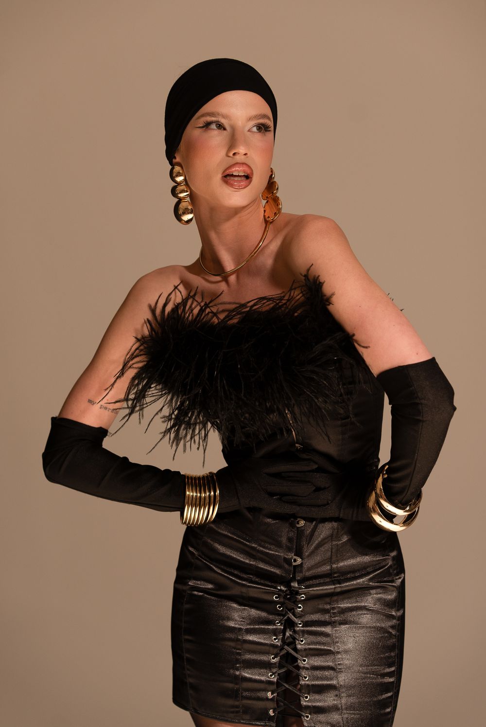 Glamorous retro fashion photo featuring black satin dress with feather trim, long gloves, gold jewelry and turban style headpiece.