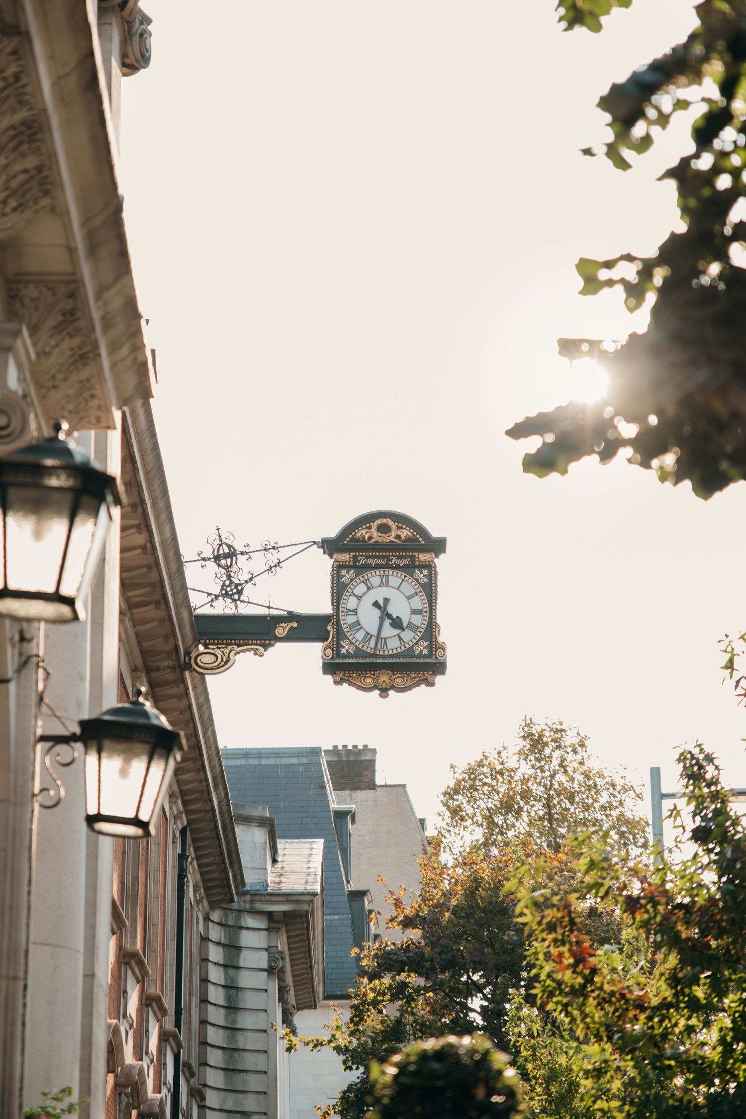 Vintage clock mounted on building exterior with decorative lanterns and foliage.