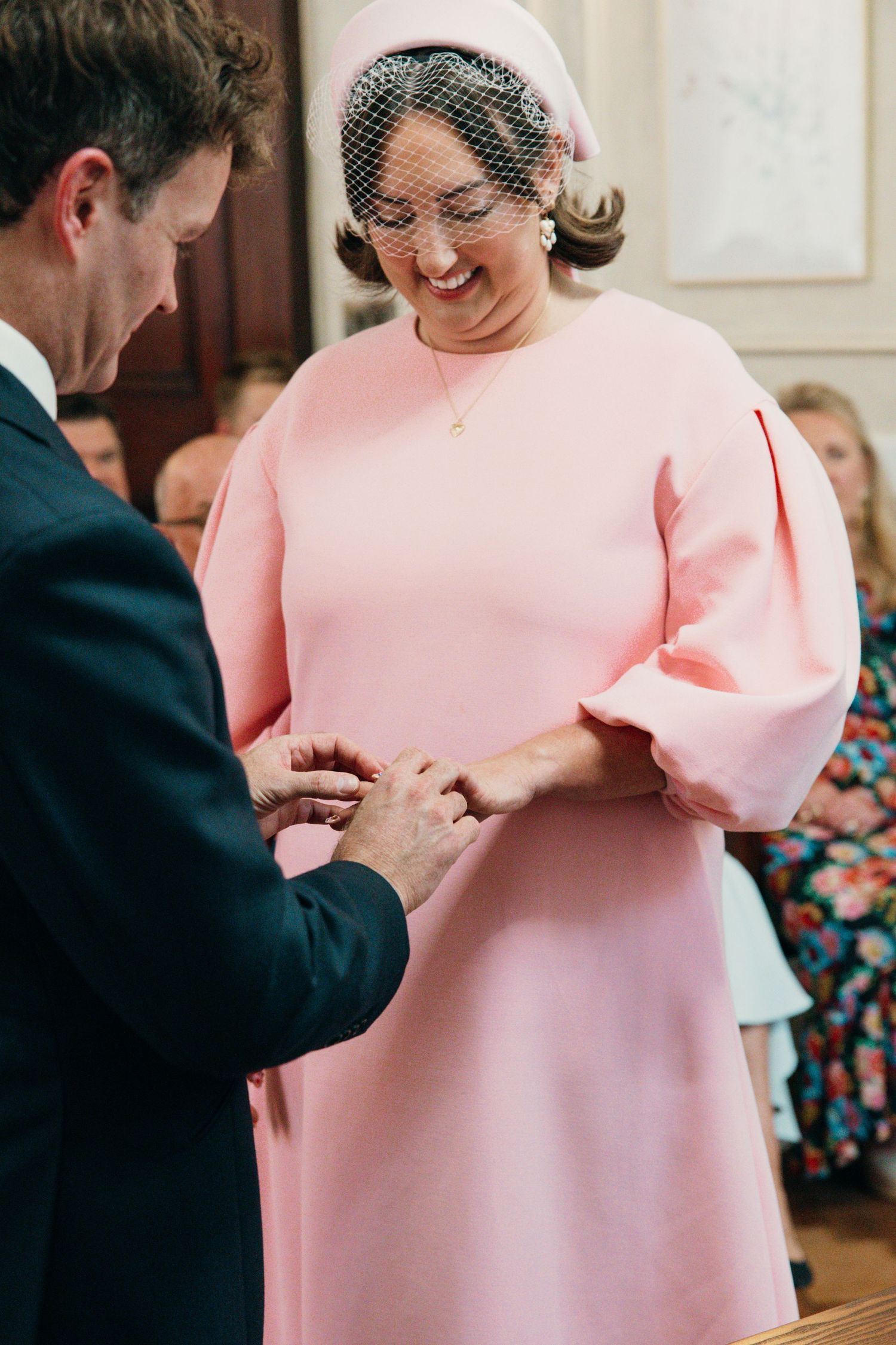 A close-up of a ring exchange during a wedding ceremony with pink dress details.
