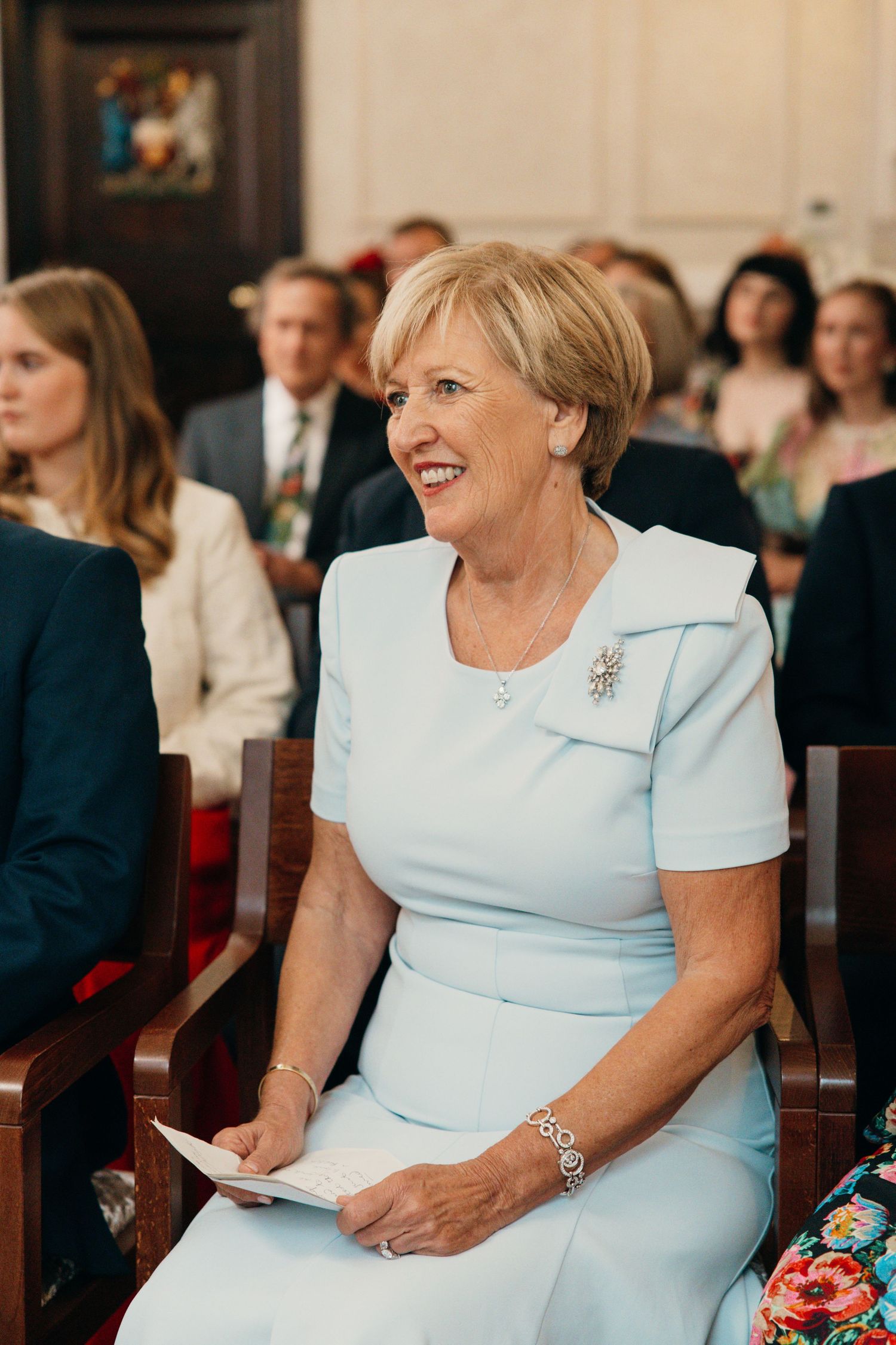 A guest in a powder blue dress smiles during a wedding ceremony.