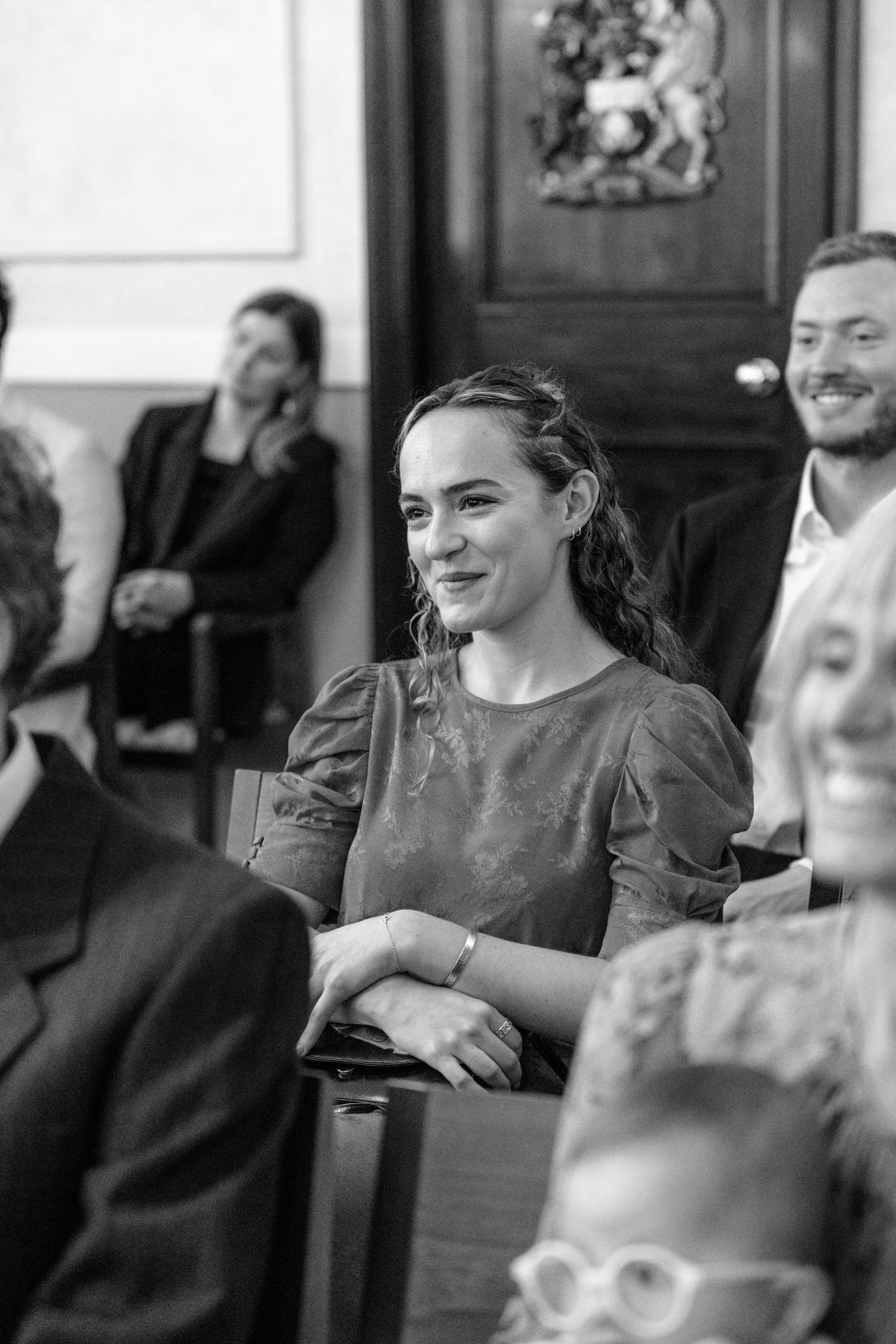A guest in grey dress smiles during an indoor wedding ceremony.