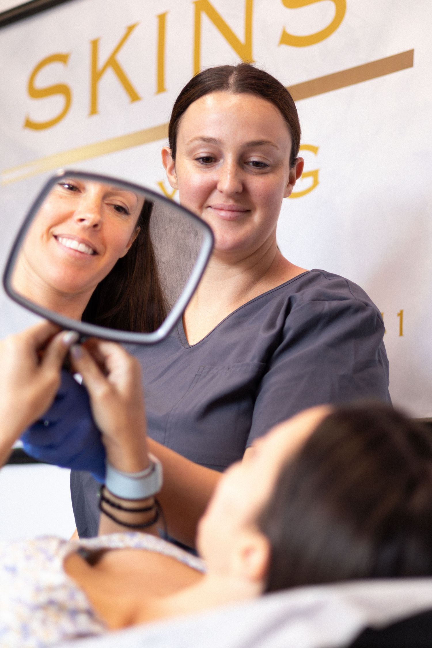 Healthcare professional in scrubs demonstrates skincare procedure using a hand mirror.
