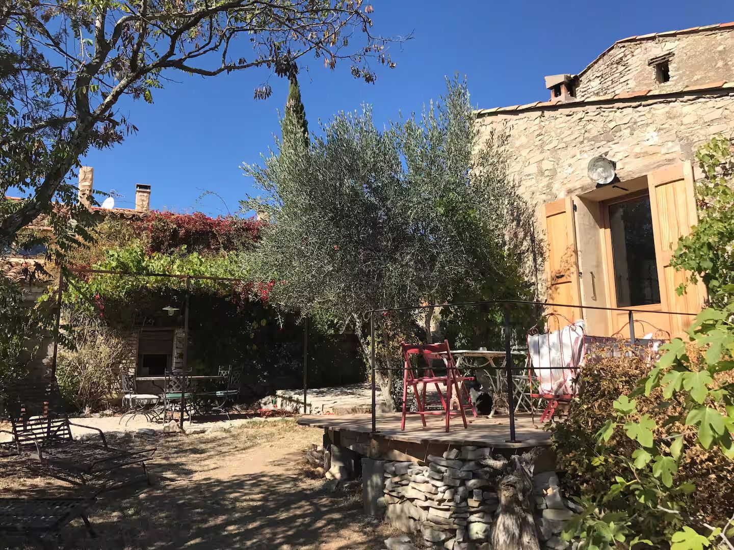 Mediterranean stone villa with olive trees and outdoor patio seating area under a sunny blue sky.