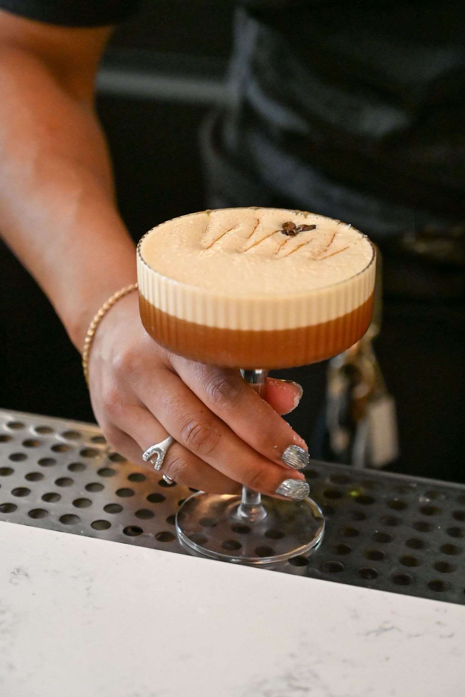 A layered espresso martini cocktail with cream foam top being served on a bar counter.