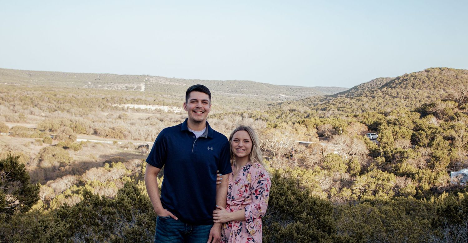 A couple enjoying a scenic overlook in a desert mountain landscape with rolling hills and vegetation in the background.