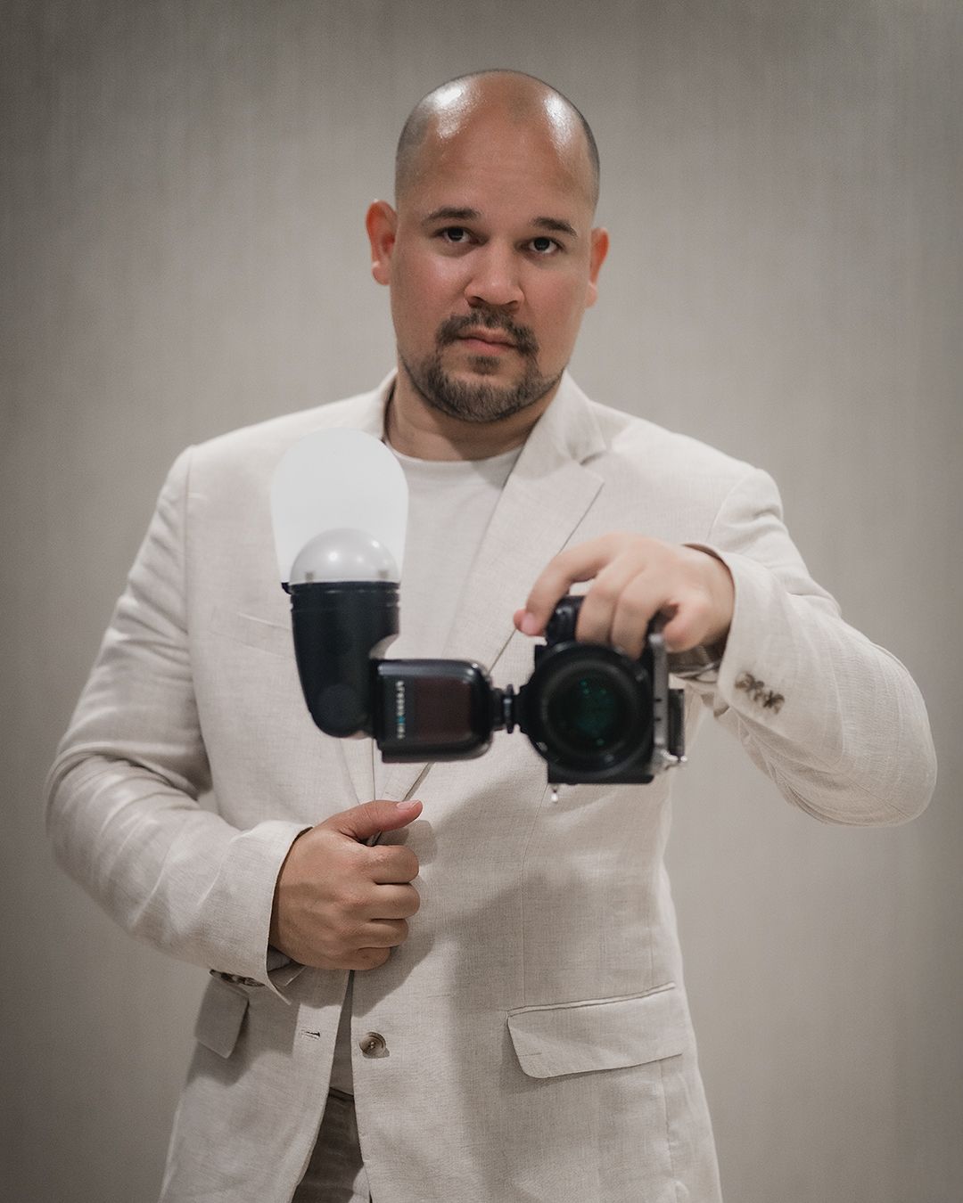 Professional photographer in a white suit jacket holding a camera with stabilizer equipment.
